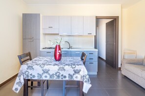 A modern kitchen with light-colored cabinets, a dining table with a patterned tablecloth, and a red vase.