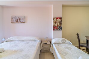 A bedroom with two beds, a nightstand with a lamp, and artwork on the walls.
