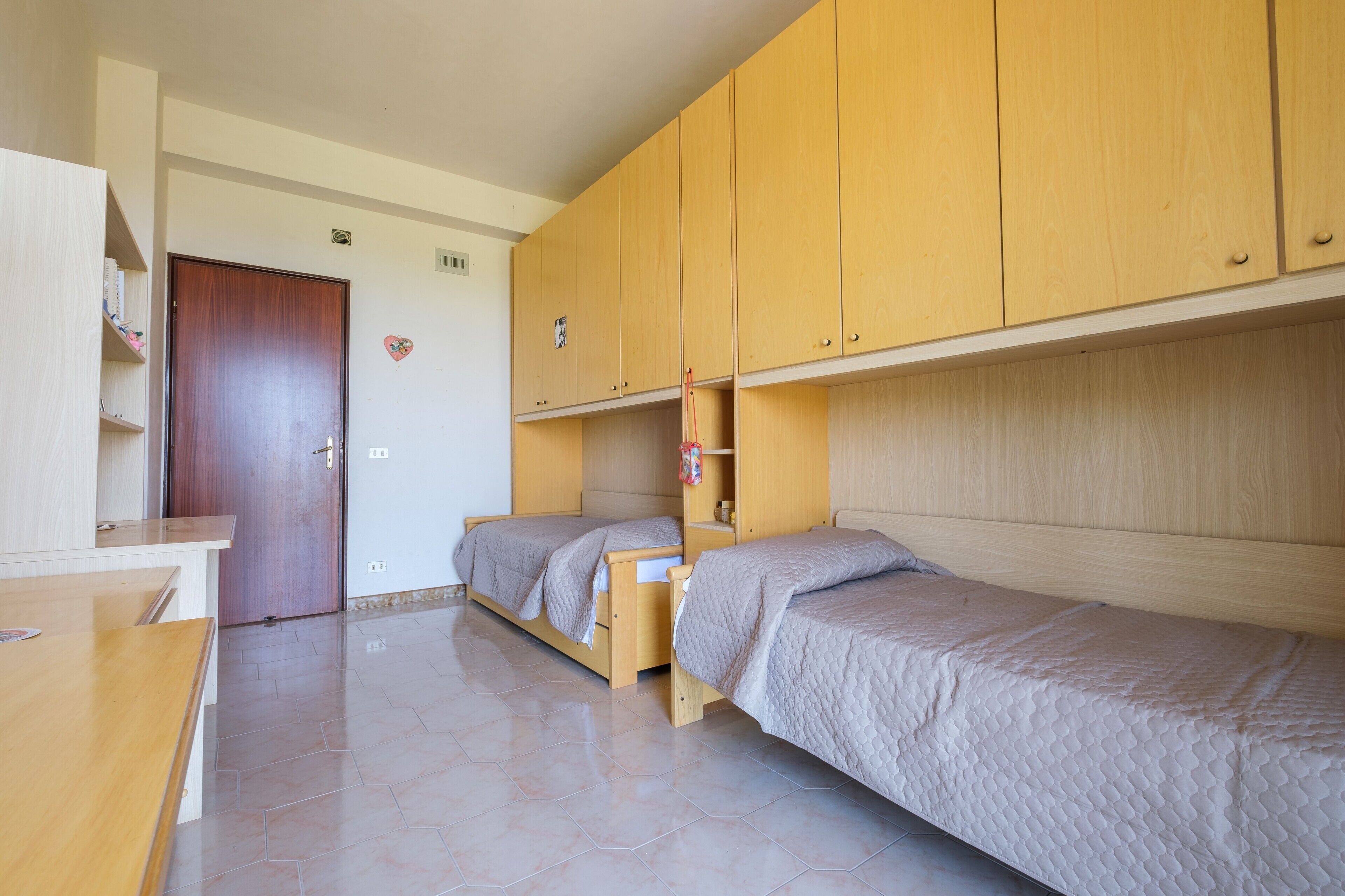 Een slaapzaal met twee eenpersoonsbedden, houten kasten, een bureau en een deur.