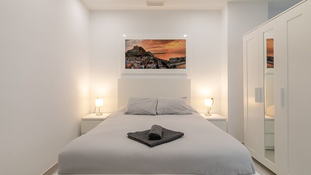 Une chambre à coucher moderne avec un lit, un tableau au-dessus, des lampes de chevet et une armoire.