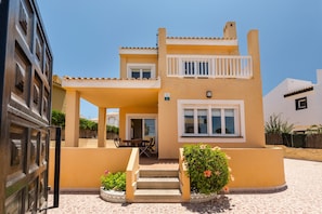 A two-story building with a balcony, a door, and a small patio area with a table and chairs.