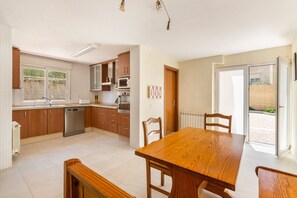 Eine moderne Küche mit Holzschränken, einem Edelstahl-Geschirrspüler und einem Essbereich mit Holztisch und -stühlen.