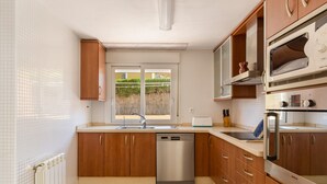 A kitchen with wooden cabinets, a dishwasher, a microwave, and a window with a view of greenery.
