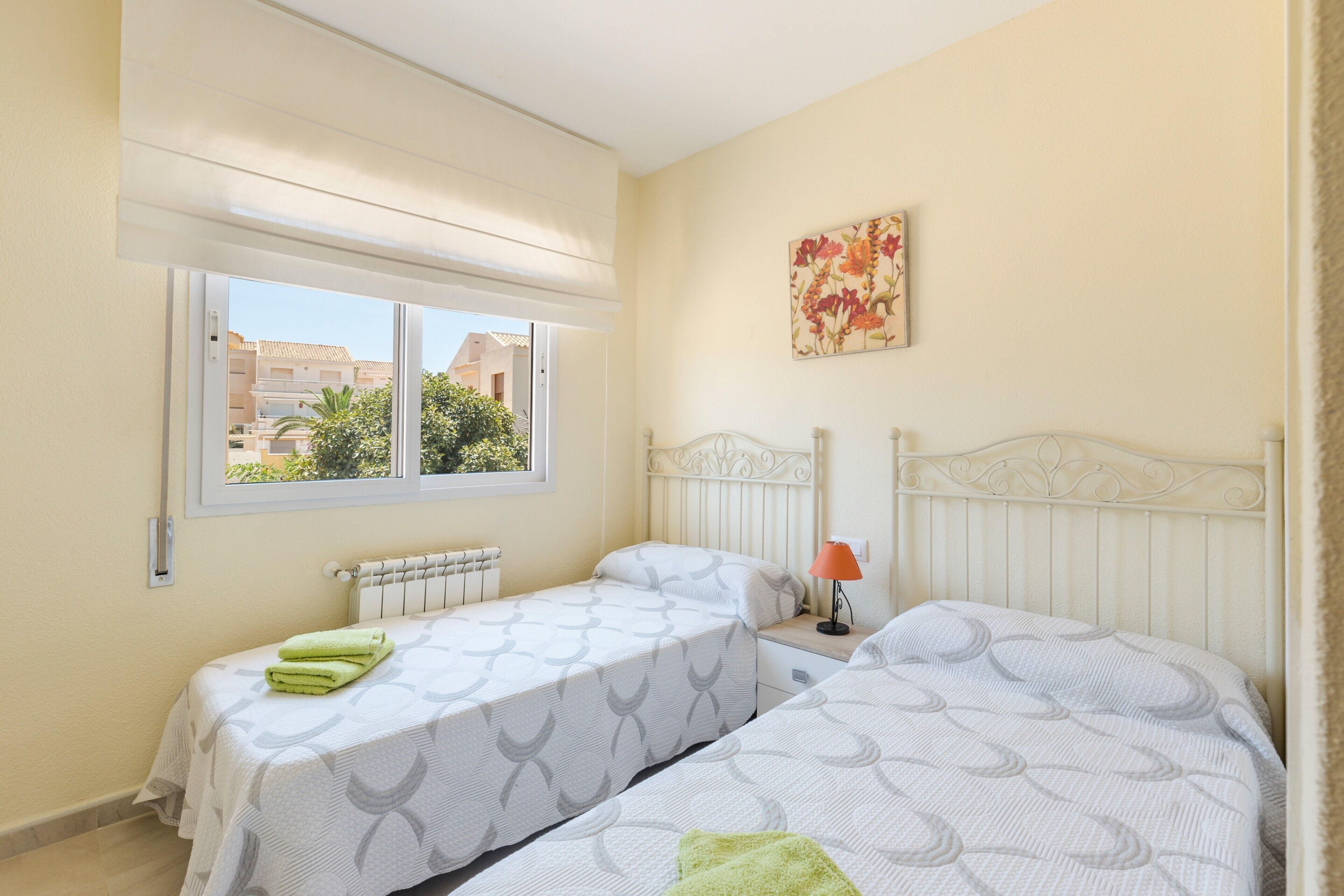 A bedroom with two beds, a window with a view, a radiator, and a painting on the wall.