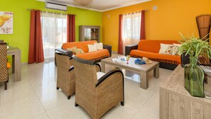 Ein Wohnzimmer mit zwei orangefarbenen Sofas, Korbstühlen, einem Holztisch und einem Fernseher.