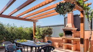 Eine Terrasse im Freien mit einem Backofen aus Ziegeln, einem Tisch mit Stühlen und einer hängenden Pflanzampel.