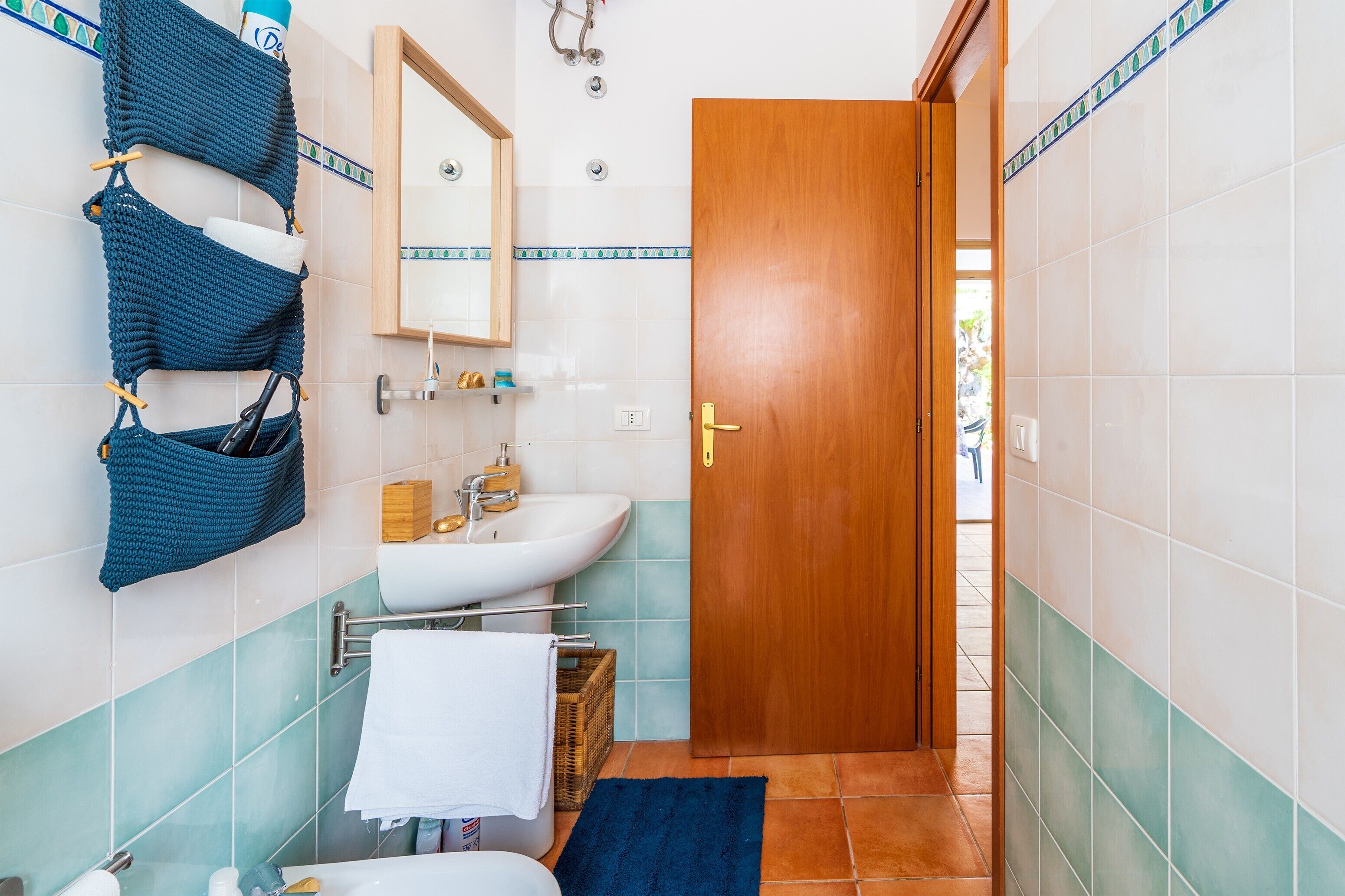 A bathroom with a wooden door, a white sink, a mirror, and a blue towel rack.