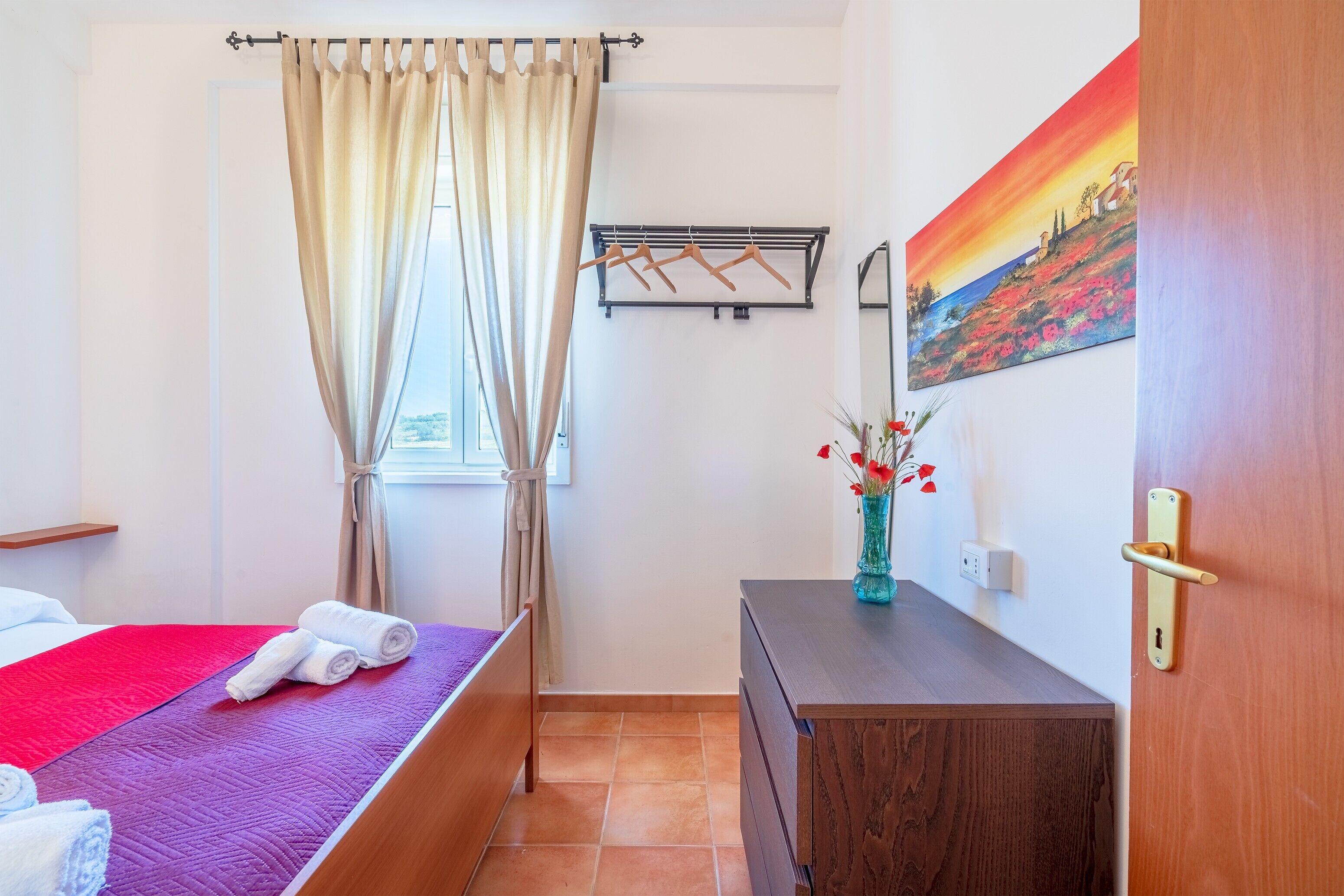Ein Hotelzimmer mit Bett, Schminktisch, einem Gemälde und einem Fenster mit Vorhängen.
