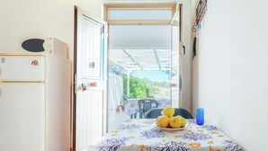 A compact kitchen with a refrigerator, a dining table with a decorative tablecloth, and a view of a covered outdoor area. - Vacation Home "San Lorenzo" with Private Terrace, Private Garden and A/C (San Lorenzo)