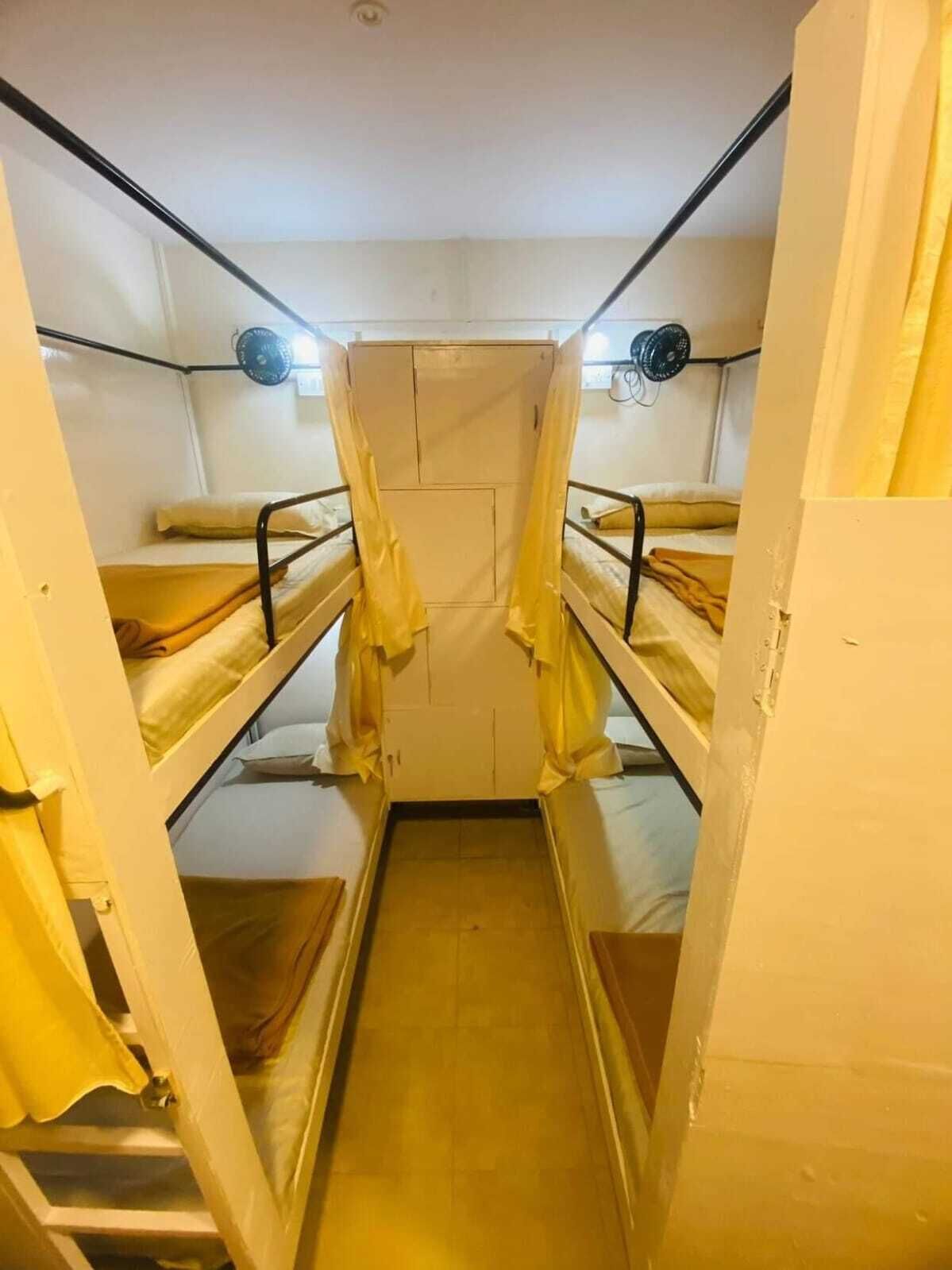 A narrow, enclosed room with bunk beds, a small window, and a door.