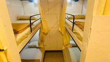 A narrow, enclosed room with bunk beds, a small window, and a door.