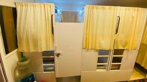 A room with two white doors, each with a yellow curtain and a window. There is a large water dispenser on the left side. - Golden Star Dormitory (Mumbai)