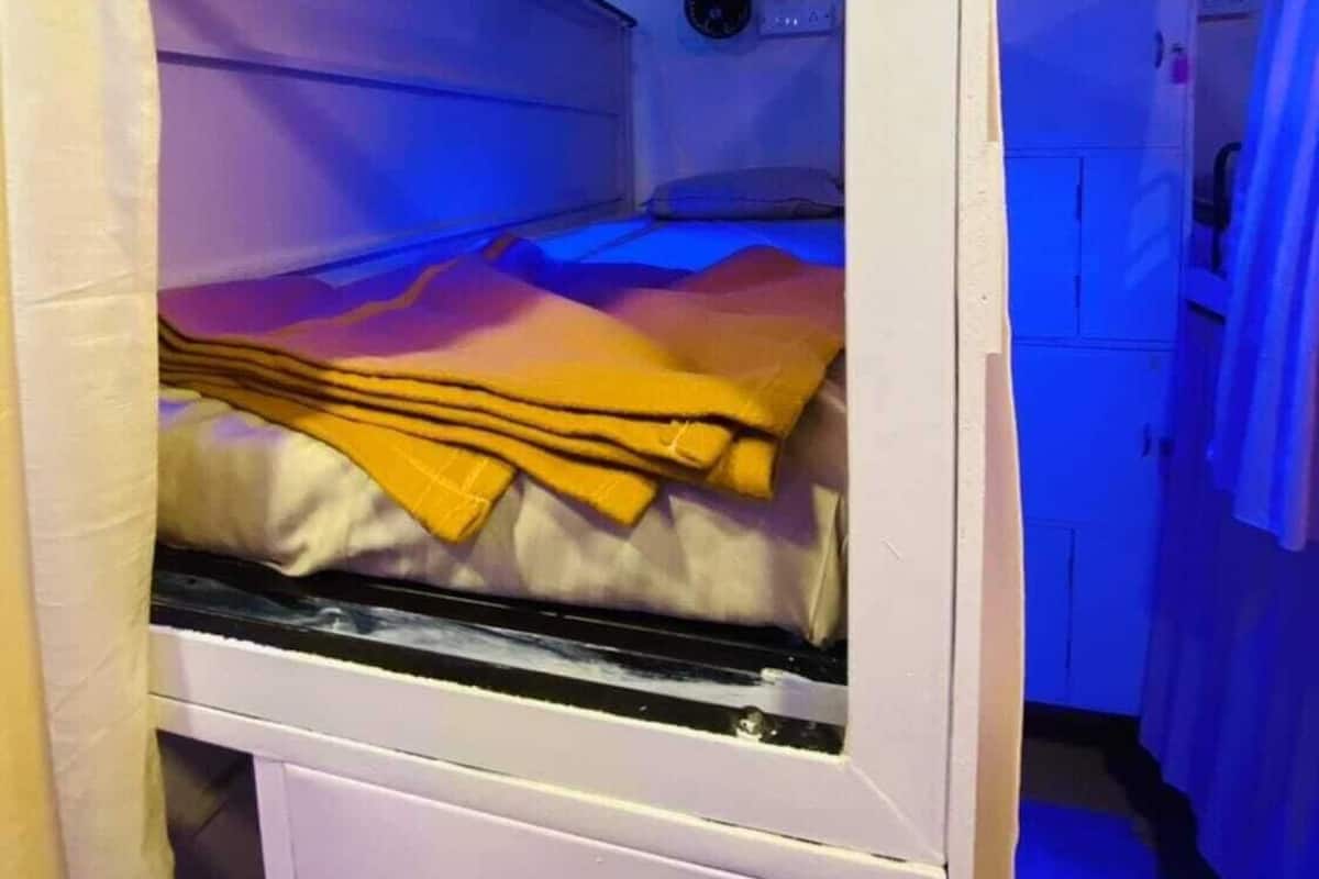 Kerrossänky patjoineen ja tyynyineen, pieni lämmitin ja seinään kiinnitetty tuuletin huoneessa, jossa on sininen valaistus.