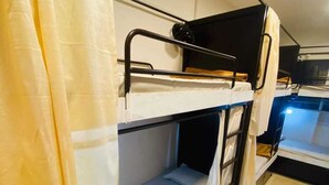 A bunk bed room with a curtain, a small table, and a tiled floor. - Golden Star Dormitory (Mumbai)