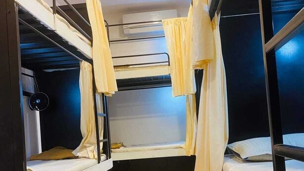 A narrow, well-lit room with bunk beds, a small table, and a fan. - Golden Star Dormitory (Mumbai)