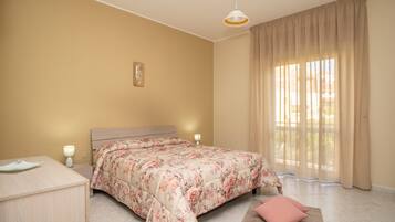 Un dormitorio con cama, lámparas de noche, mesita de noche, ventana con cortinas e imagen colgada en la pared.