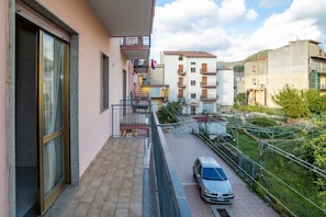 En bostadsbyggnad med balkonger, en bil parkerad på gatan och en klar himmel.