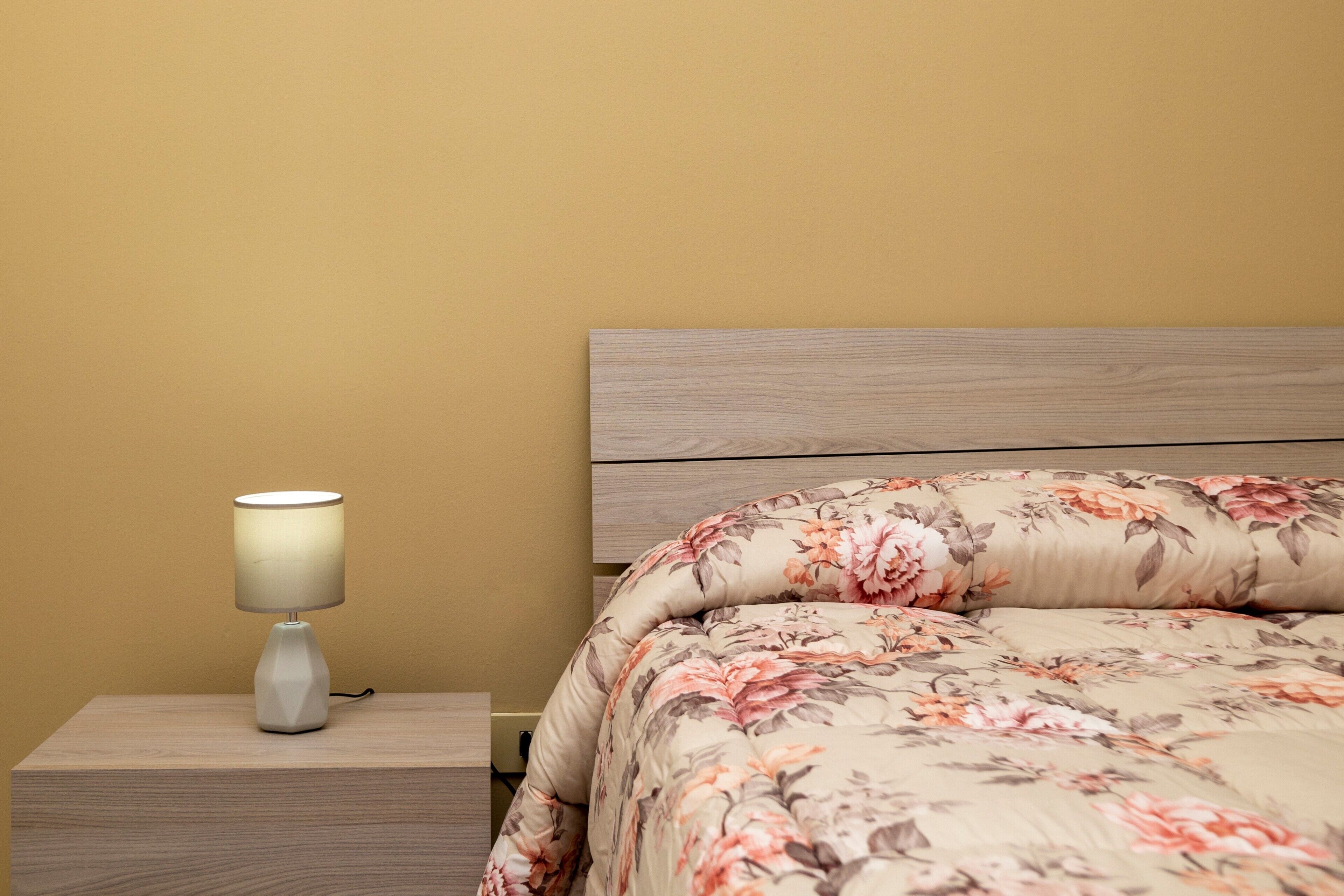 A bed with floral bedding, a bedside lamp, and a wooden headboard.