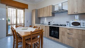 A modern kitchen with wooden cabinets, a dining table with chairs, a built-in oven, and a microwave.