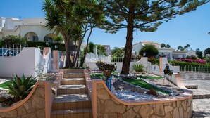 Un espace aménagé avec des marches menant à un bâtiment, entouré de palmiers et délimité par une clôture blanche.