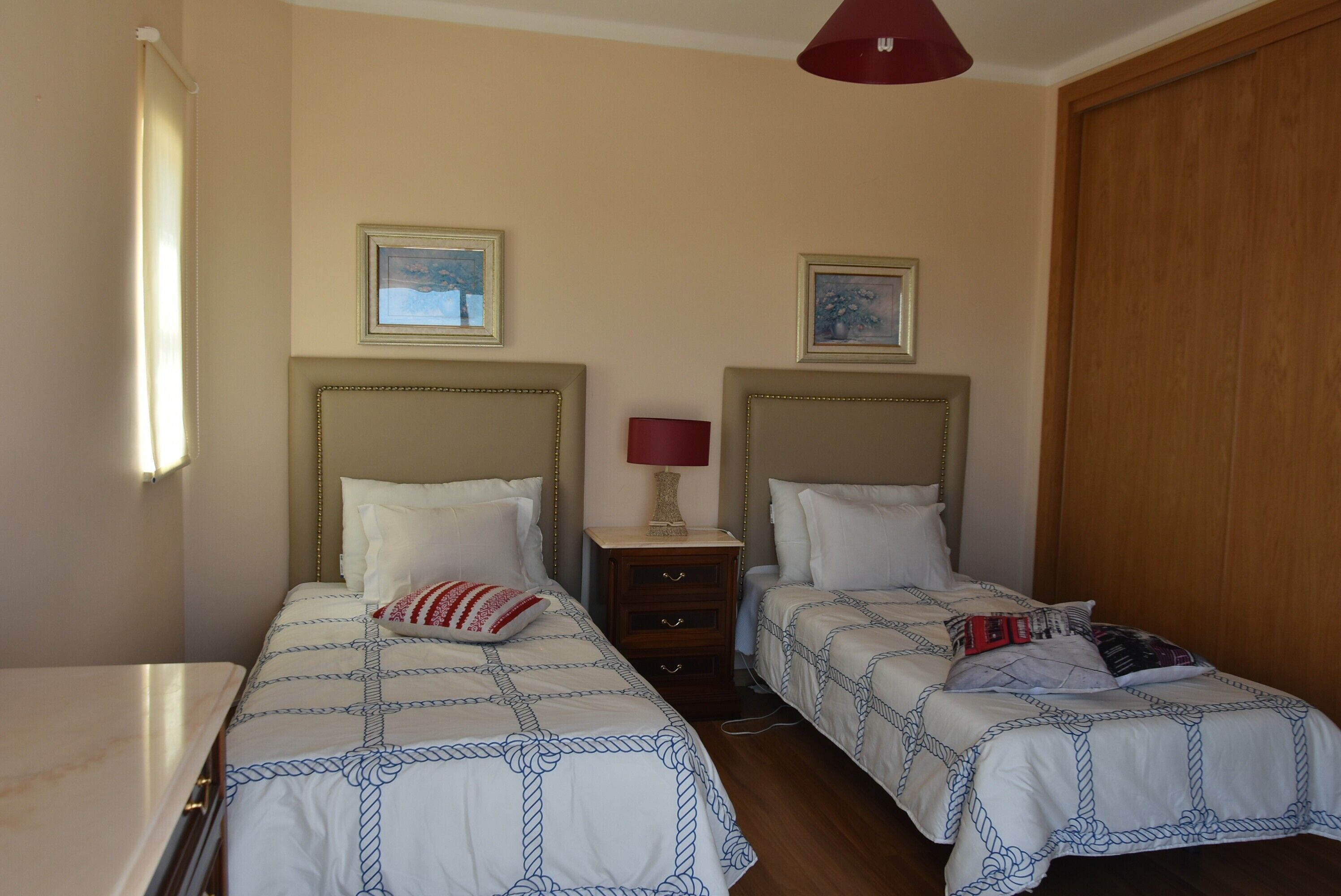 Una habitación con dos camas, una mesita de noche, una lámpara y dos cuadros en la pared.