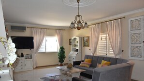Un salon avec un canapé gris, une table basse, un téléviseur, une plante en pot et un lustre.