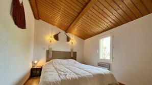 A bedroom with a wooden ceiling, a bed with a white duvet, two wall-mounted lamps, a nightstand with a lamp, and a window with a view of trees. - House for 4 with Wifi near the beach in Dolus-d'Oléron (Dolus-d'Oléron)