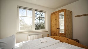 A bedroom with a bed, a wooden wardrobe, and a window with a view of trees. - Die Ferienwohnung Nr. 02 in der Villa am Sonnenhang (Göhren)