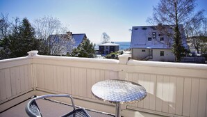 A balcony with a round table and a chair, overlooking a residential area with houses and a view of the ocean. - Die Ferienwohnung Nr. 02 in der Villa am Sonnenhang (Göhren)