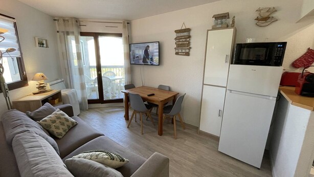 A compact living space with a sofa, dining table, chairs, a TV, a microwave, and a refrigerator. - Saint-Cyprien: Renovated T2 cabin for 6, pool, parking, 100m from the beach (Saint-Cyprien)
