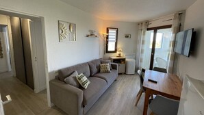 A living room with a sofa, a dining table, a TV, and a window with curtains. - Saint-Cyprien: Renovated T2 cabin for 6, pool, parking, 100m from the beach (Saint-Cyprien)