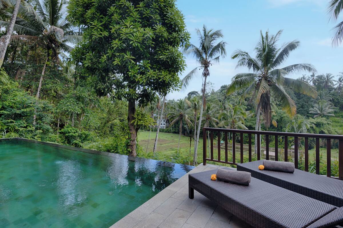 A poolside area with wicker lounge chairs and a view of a lush garden.