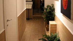 En smal gang med en dør til venstre, en potteplante i midten og kunst på højre væg.
