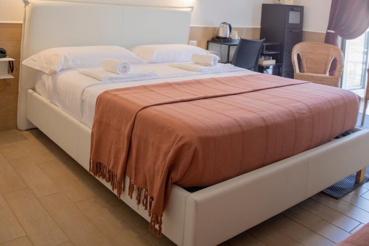 A hotel room with a large bed, a desk, a chair, and a painting on the wall.