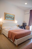 Una camera d'albergo con un letto grande, una scrivania, una sedia e un quadro appeso al muro.