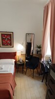 A hotel room with a bed, a desk, a chair, a lamp, a mirror, and a framed picture on the wall.