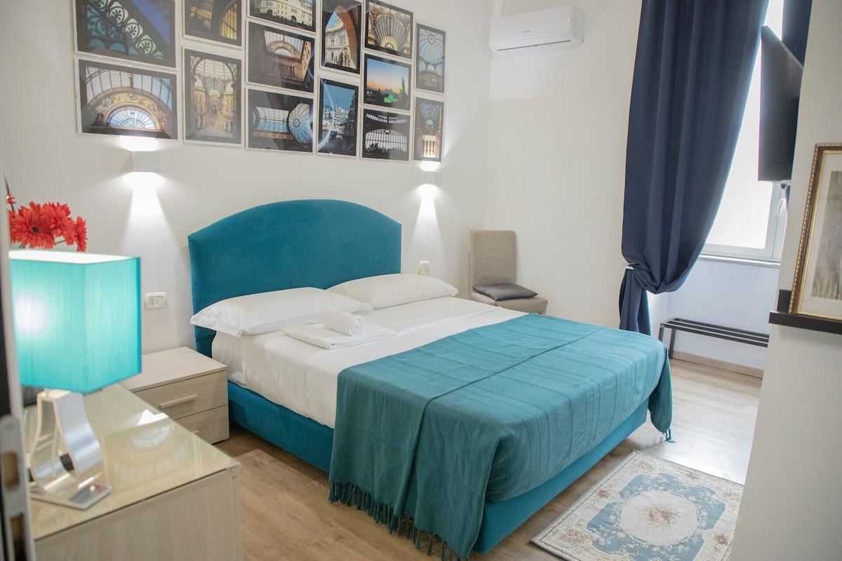 A neatly arranged bedroom with a bed, bedside tables, a lamp, a chair, and a wall with framed pictures.