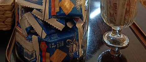 A room with a coffee station featuring a jar of biscotti, stacked paper cups, and a glass with biscotti packets.