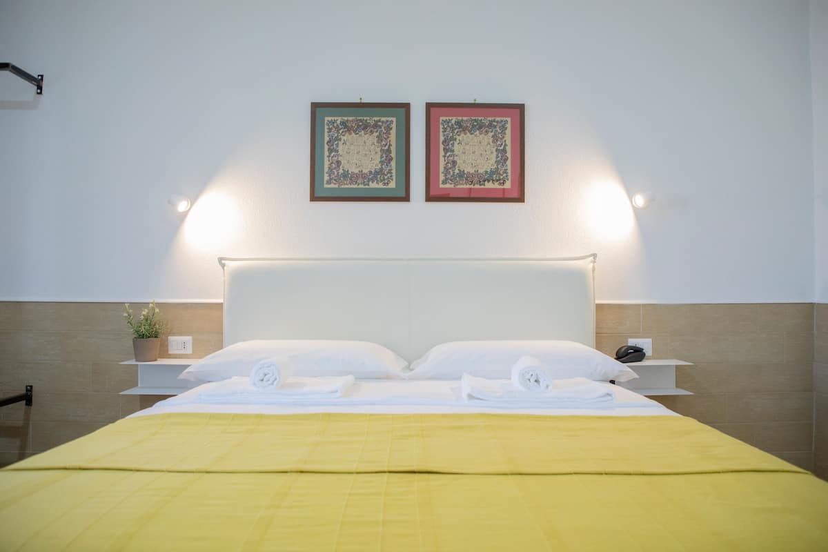 A neatly made bed with a yellow bedspread, two bedside tables with lamps, and two framed pictures on the wall.