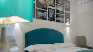 Una habitación de hotel con una cama grande, cabecera, mesita de noche, lámpara, silla y una pared con cuadros.