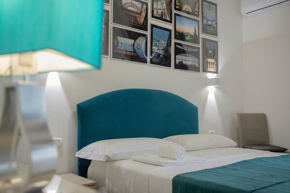 A hotel room with a large bed, a headboard, a nightstand, a lamp, a chair, and a wall with framed pictures.