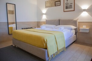 Un letto rifatto con una coperta gialla, un comodino con una lampada e un punto luce a parete.