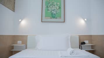 Una camera d'albergo con un letto, lenzuola bianche, un quadro floreale incorniciato sulla parete, comodini con lampade e un telefono su uno dei tavoli.