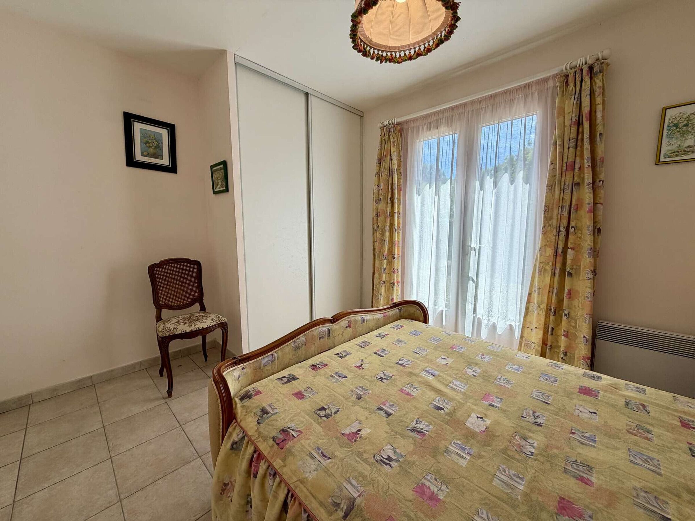 Una stanza con un letto, una sedia, un termosifone e una finestra con tende.