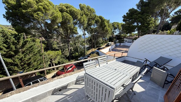 Une terrasse sur le toit, avec une table et des chaises, entourée d’arbres et offrant une vue sur les voitures garées.