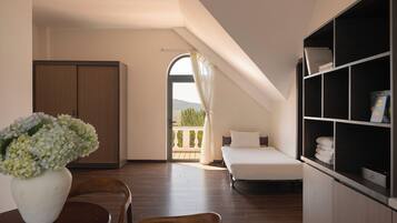 A bedroom with a bed, a wardrobe, a desk with a chair, a bookshelf, and a view of a balcony.
