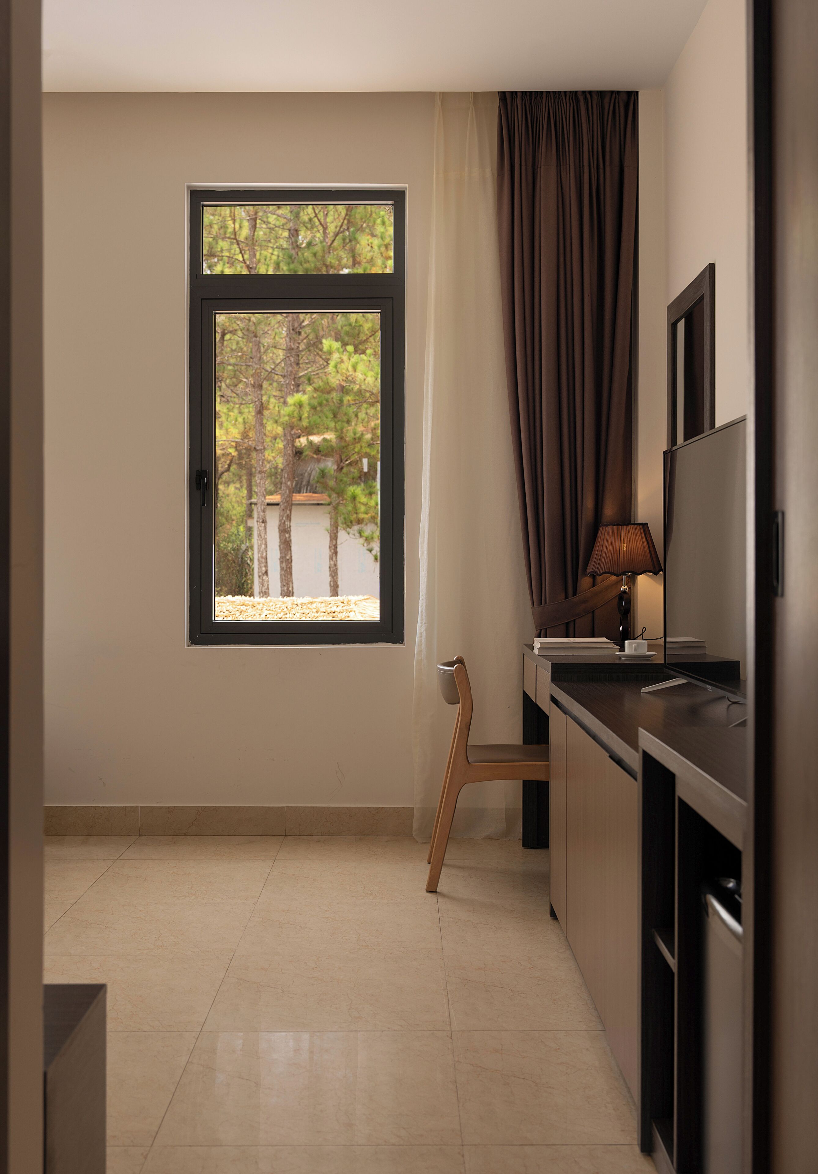 A small, modern room with a window, a desk, a chair, and a television.