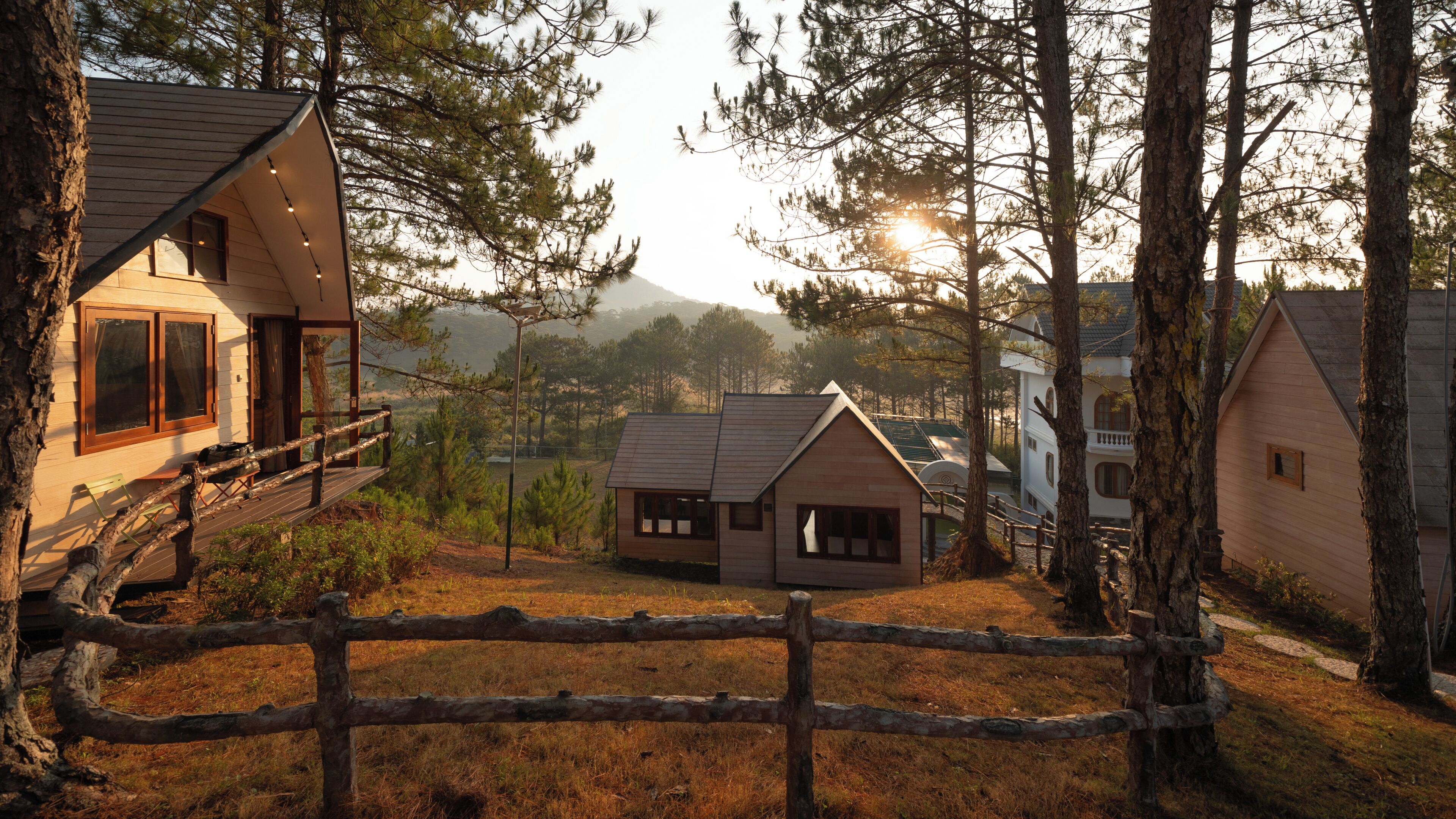 A cabin with a deck, surrounded by trees and a mountain in the background.