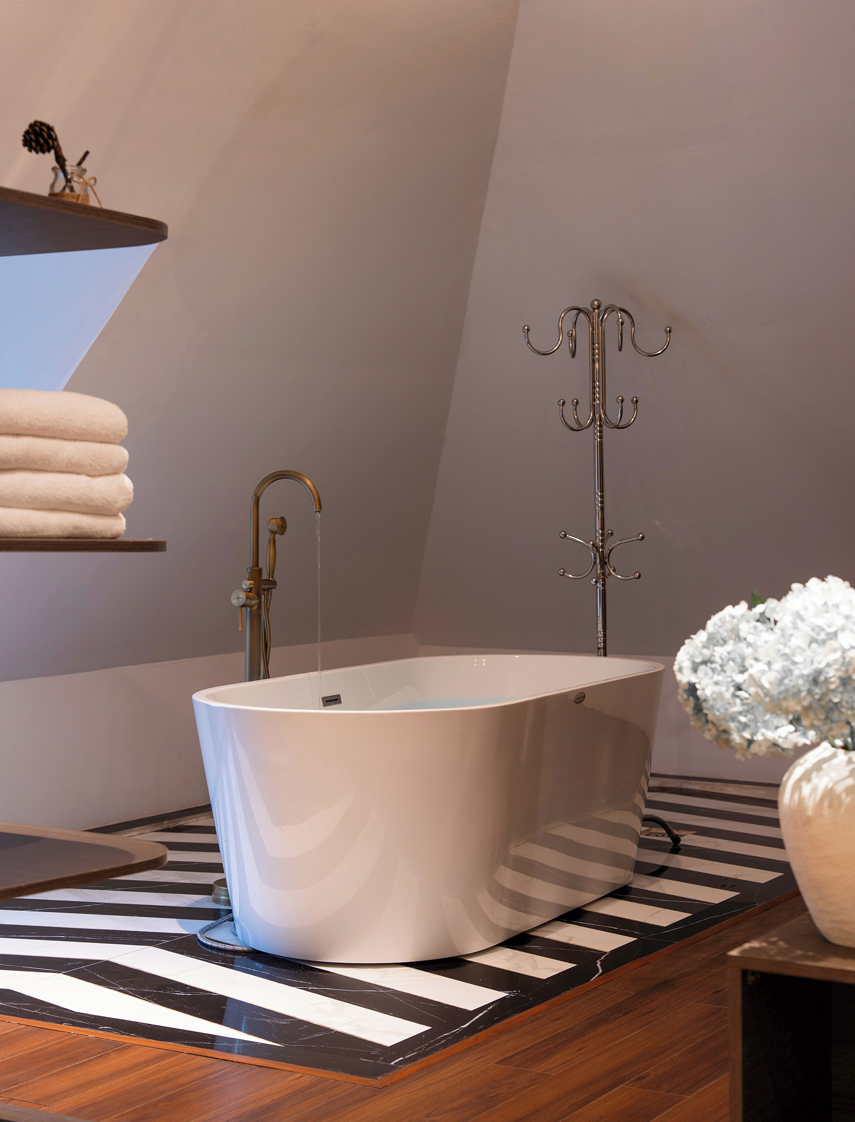 A modern bathroom with a freestanding bathtub, a towel rack, and a vase with flowers.