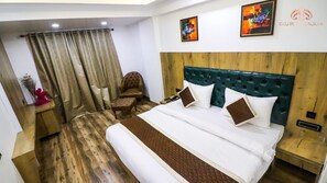 Ein Hotelzimmer mit einem großen Bett, einem Holzkopfende und Holzboden. An der Wand hängen zwei Gemälde, ein Sessel und ein kleiner Tisch mit einer Blumenvase.